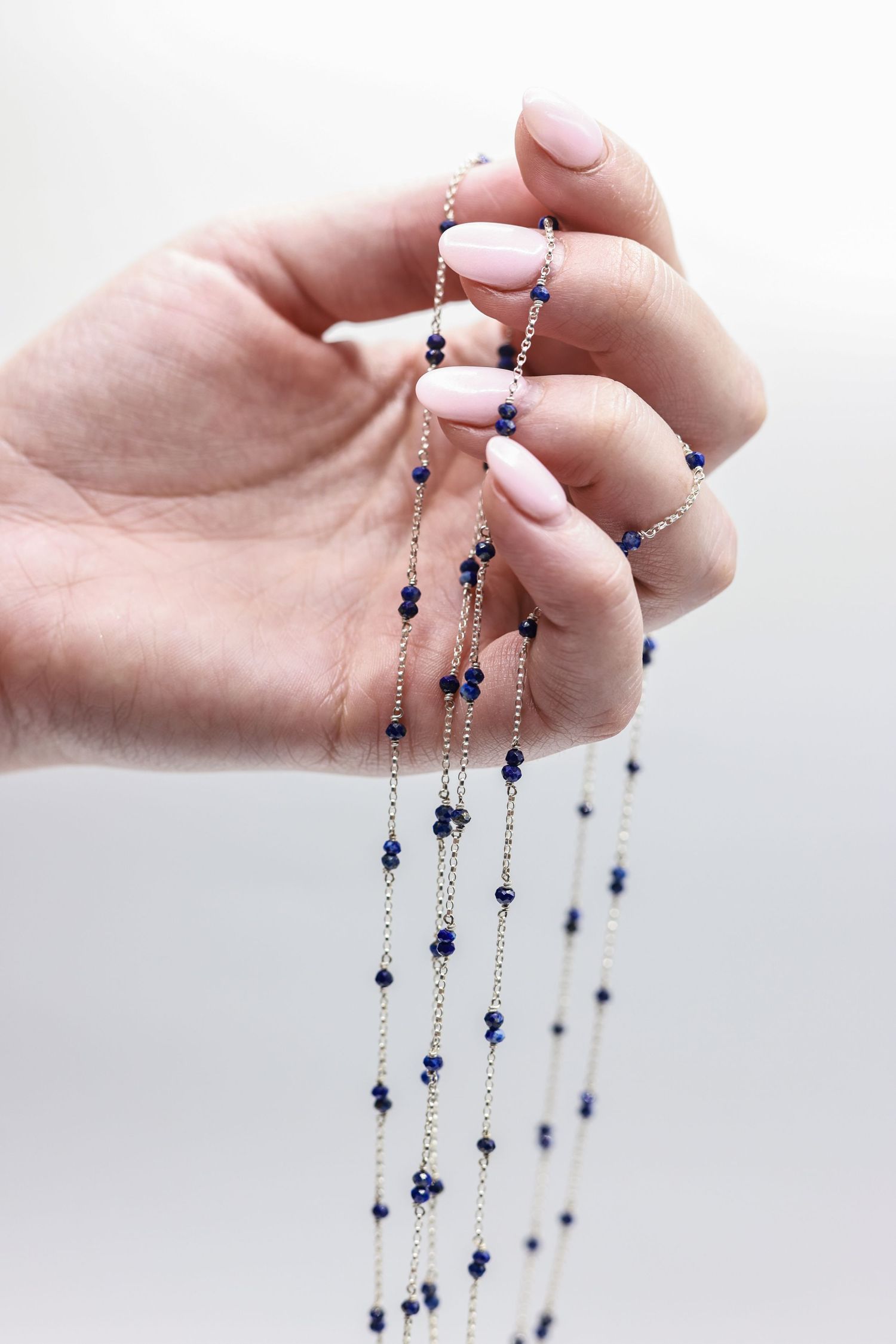 Hand holding delicate silver chain necklace with blue beads against white background.