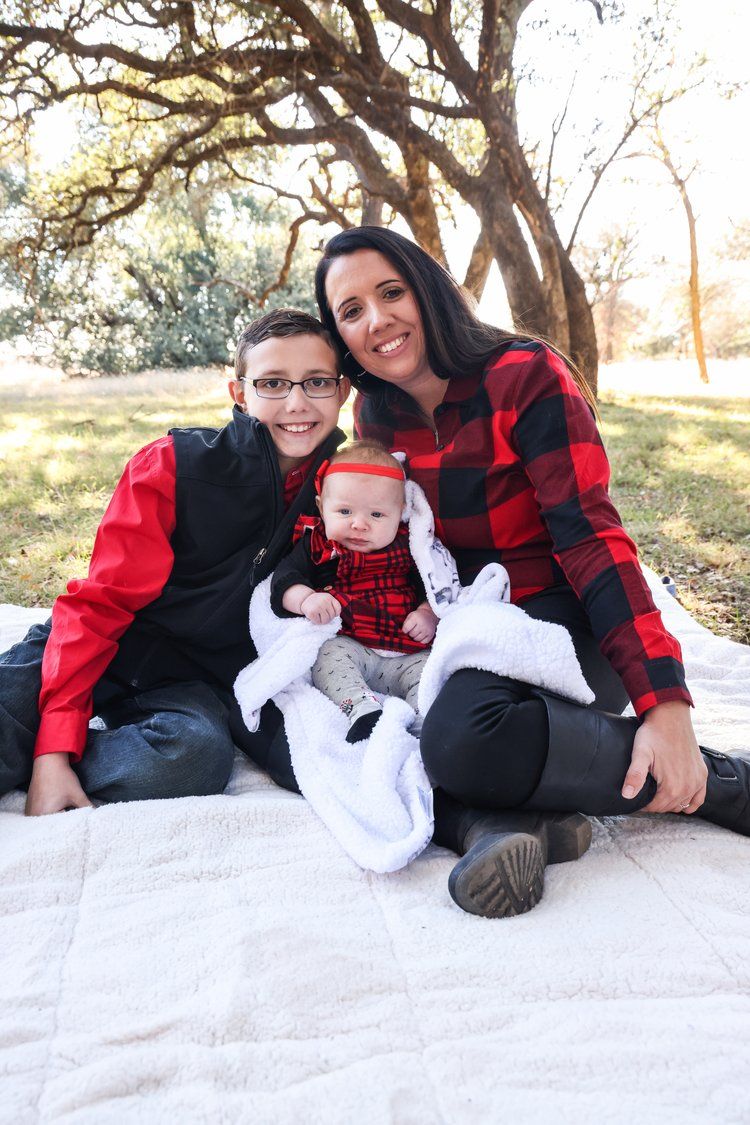 Family in matching red buffalo plaid outfits sitting on white blanket for holiday photo session in Abilene, Texas.