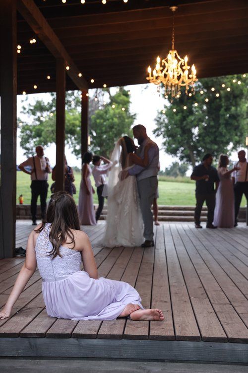A dance floor moment at a rustic wedding reception with a chandelier and guests looking on.