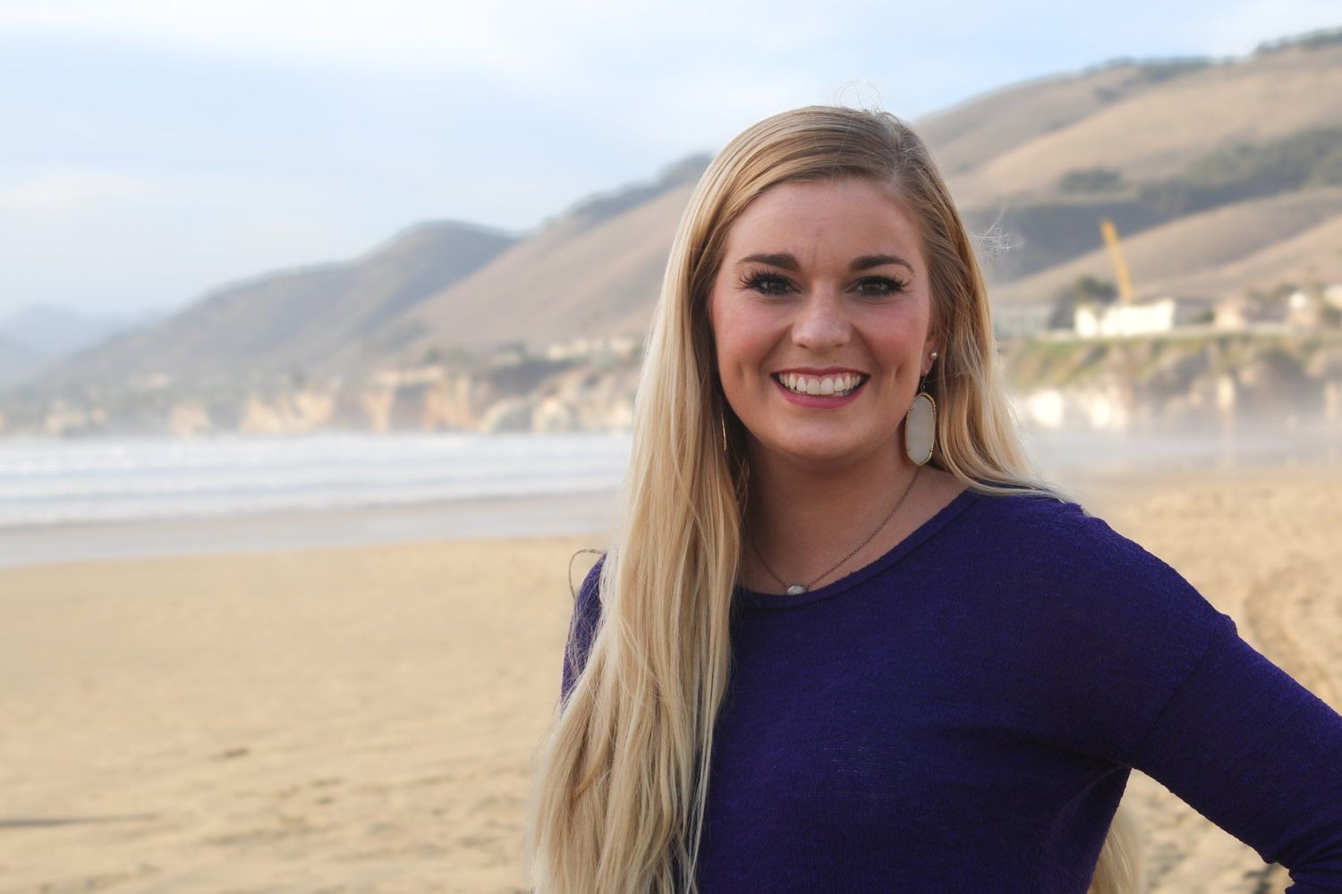 Beachside portrait with coastal mountains and waves in background.