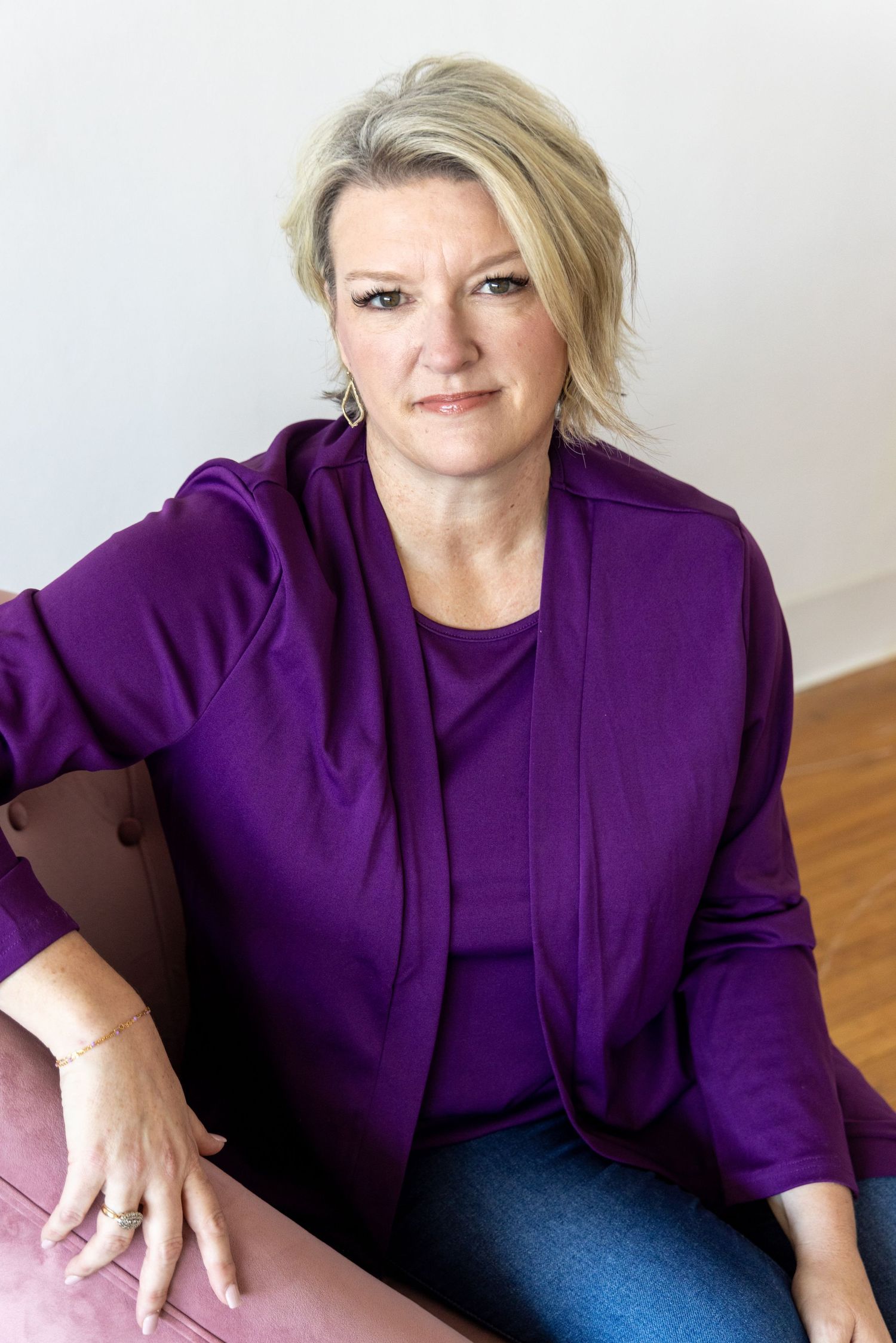 Professional headshot of a woman wearing a purple blazer sitting on pink furniture in Abilene, Texas.