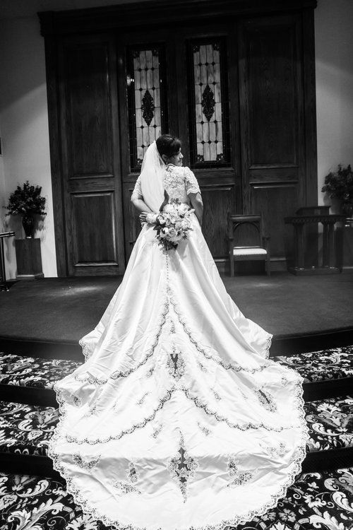 A dramatic black and white photo of a bride in a long train wedding dress from behind.
