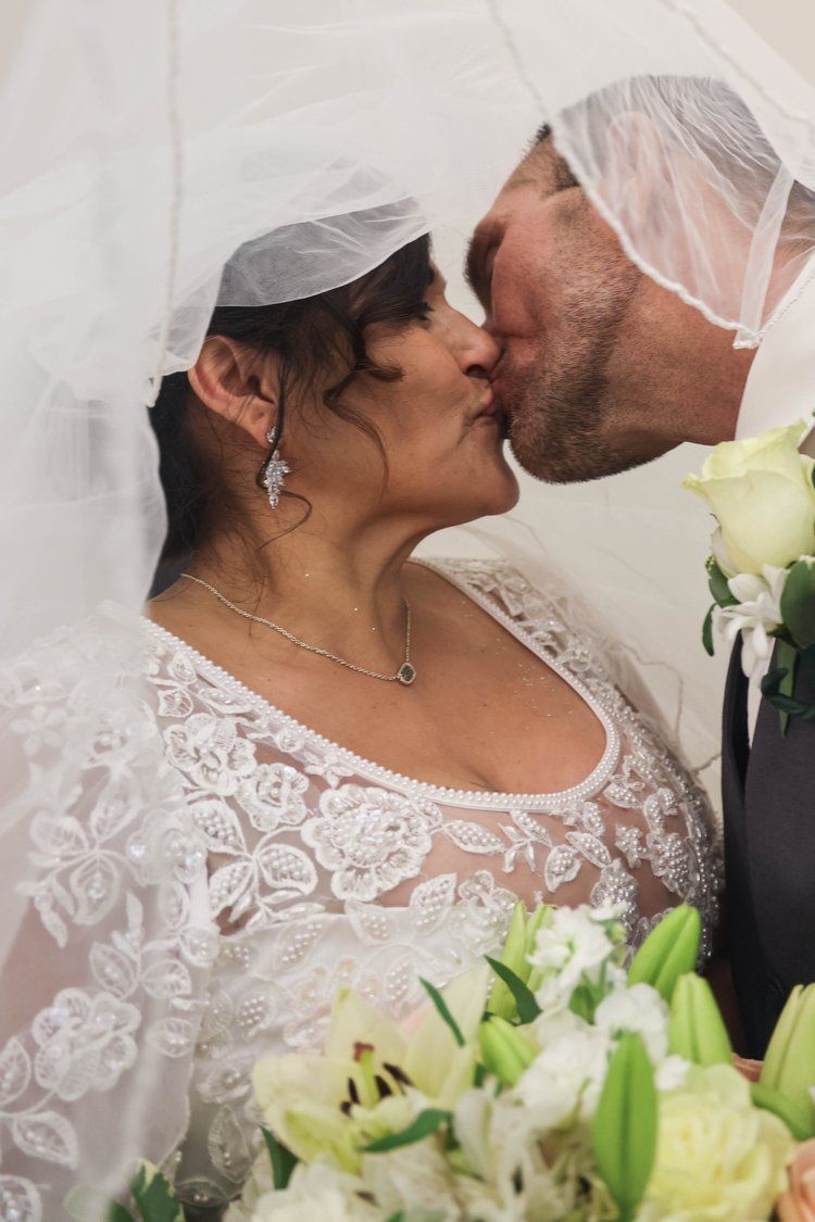 Romantic wedding moment captured under a white veil with white lilies in the foreground in Abilene, Texas.