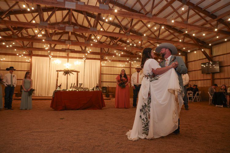 A couple shares their first dance in a rustic barn venue with string lights overhead in Abilene, Texas.