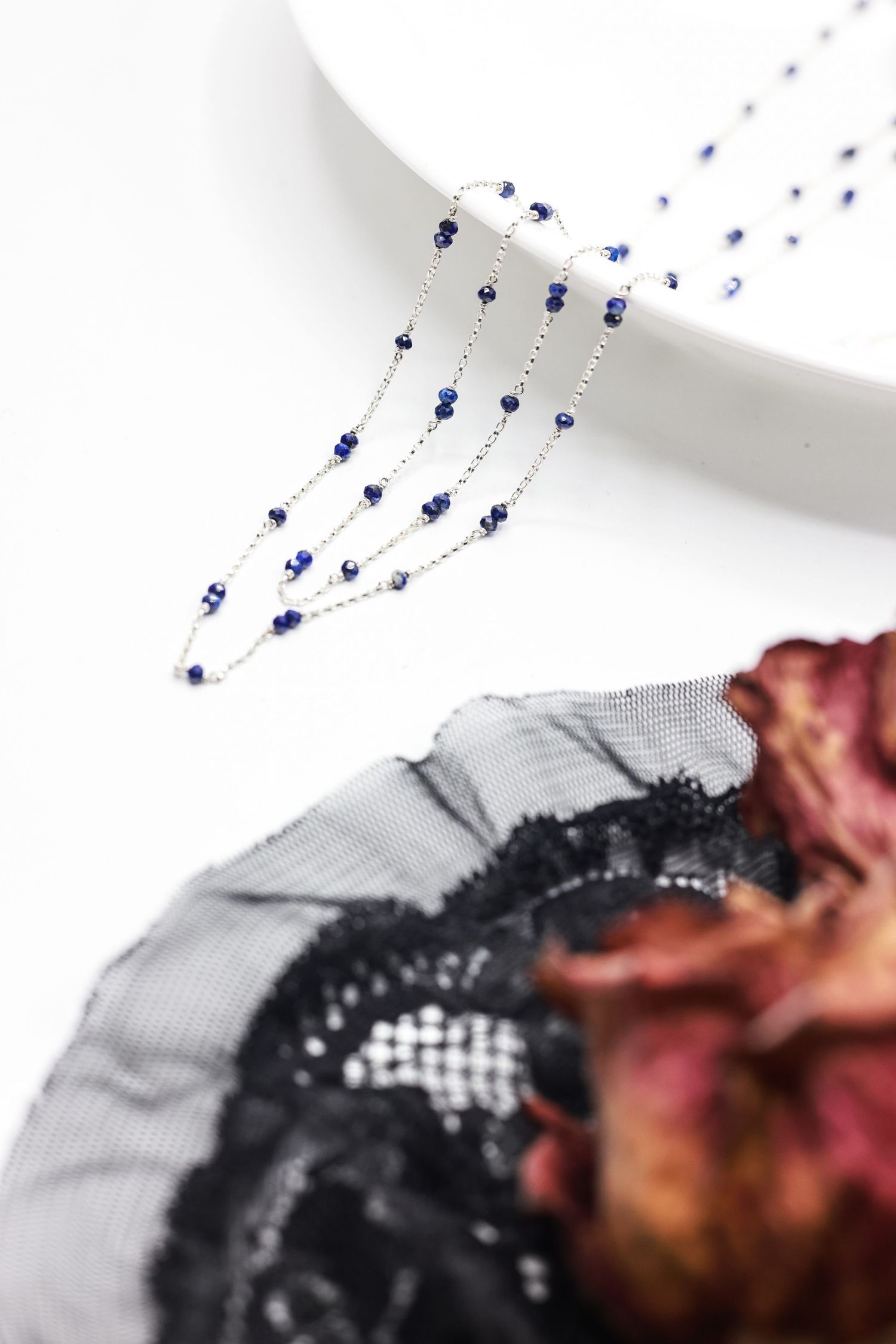 Delicate silver chain necklace with small blue beads displayed on white surface.