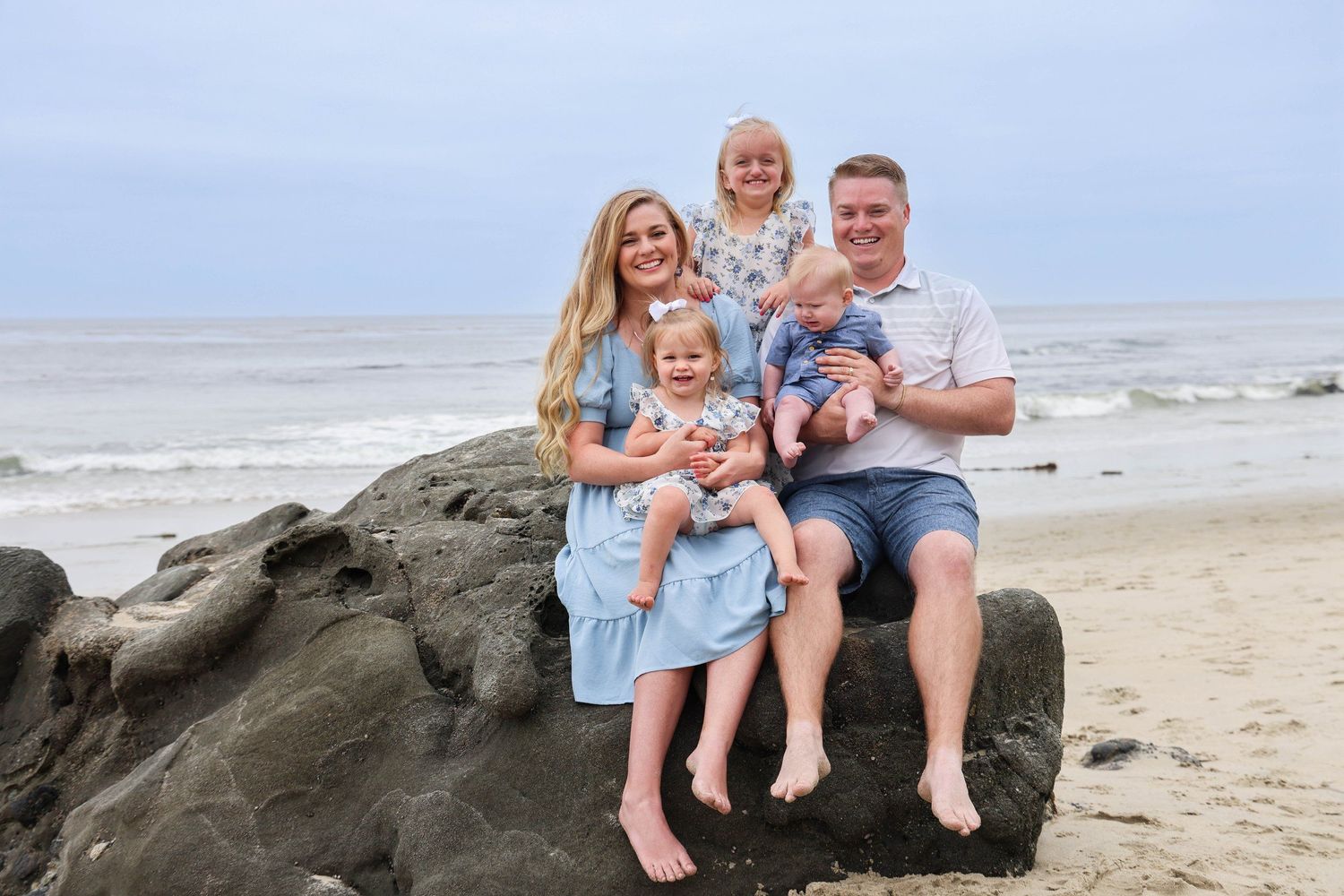 Family group seated together on rocky beach overlooking ocean waves.
