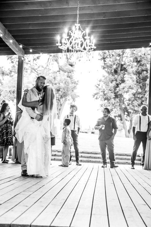 Wedding couple sharing their first dance under a crystal chandelier on an outdoor wooden deck.