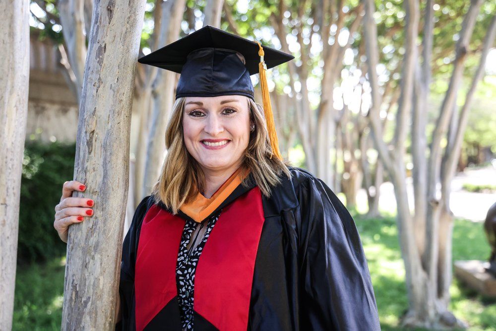 Graduate in cap and gown smiles while posing outdoors among trees in Abilene, Texas.