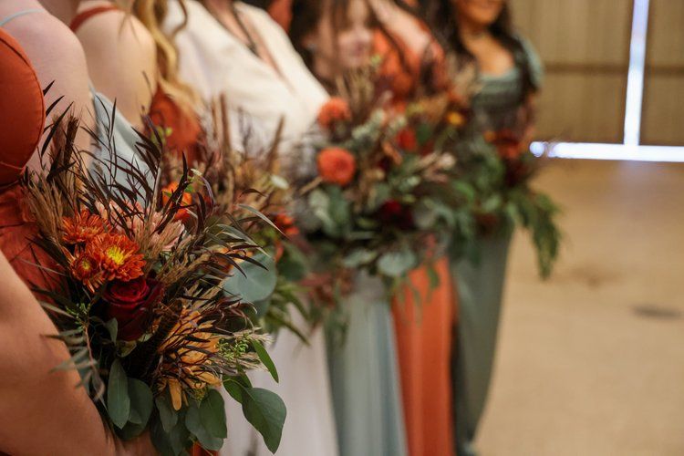 Row of bridesmaids holding autumn-themed bouquets with orange flowers and greenery in Abilene, Texas.