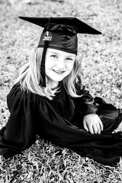 Black and white portrait of graduate in cap and gown sitting on grass in Abilene, Texas.