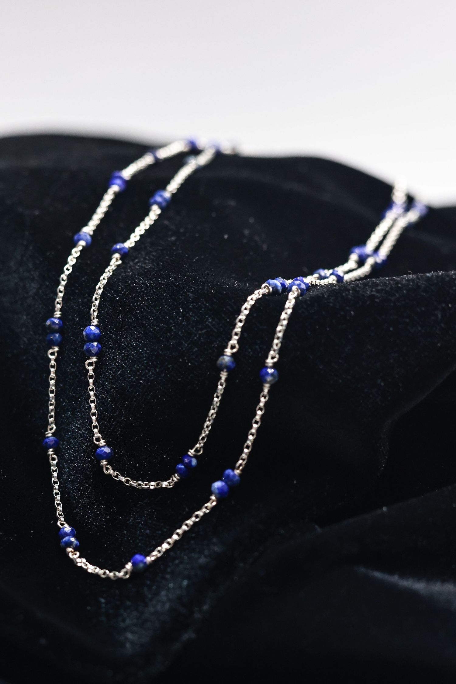 Elegant silver chain necklace with blue beads laid on black velvet surface.