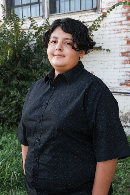 Person in black outfit poses against white brick wall with climbing vines in Abilene, Texas.