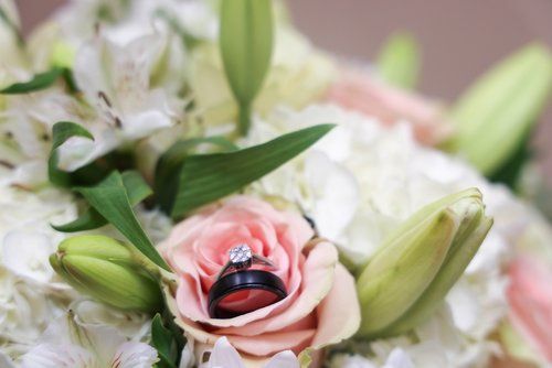 Wedding rings nestled in a pink rose surrounded by white lilies and greenery.