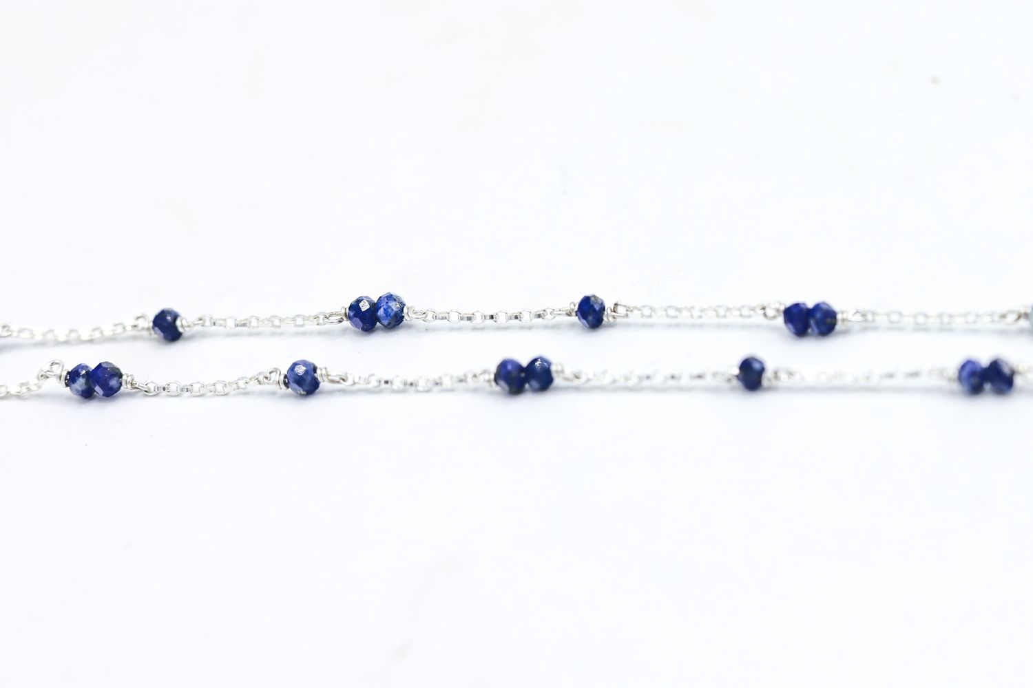 Close-up of silver chain necklace with small blue sapphire beads against white background.
