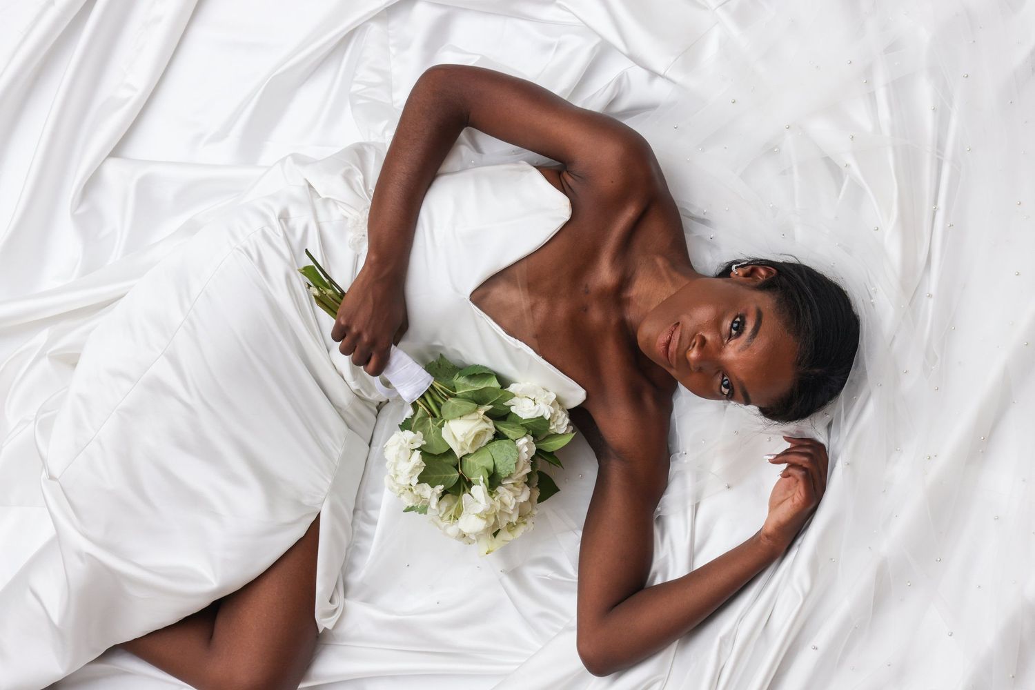 Artistic bridal portrait with white roses against white satin wedding dress in Abilene, Texas.