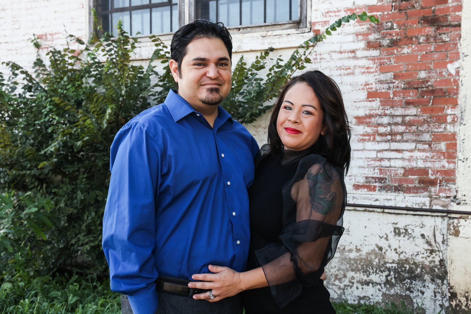 A couple poses against a rustic brick wall with climbing vines in Abilene, Texas.