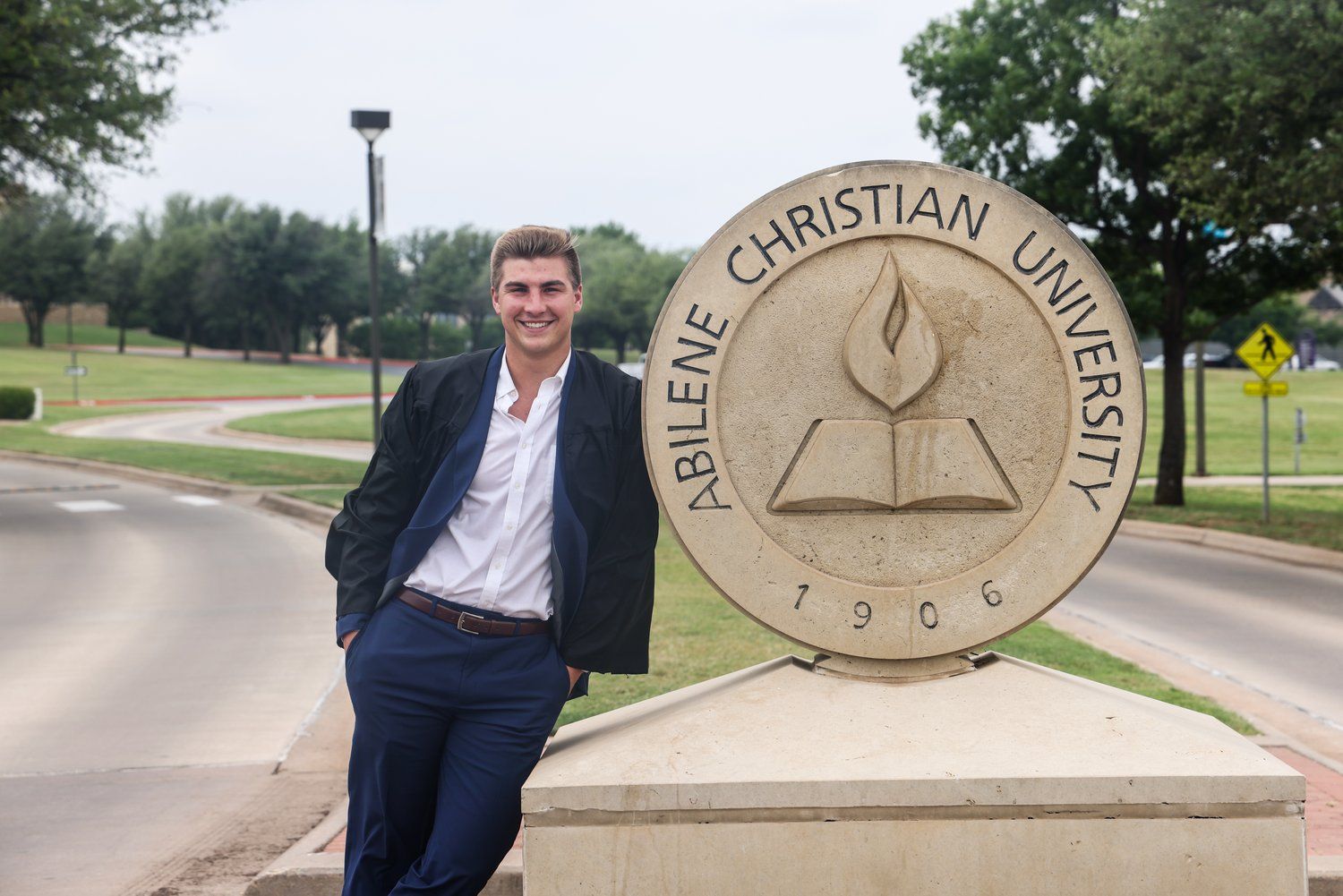 Person in suit leaning against large Abilene Christian University seal monument outdoors in Abilene, Texas.