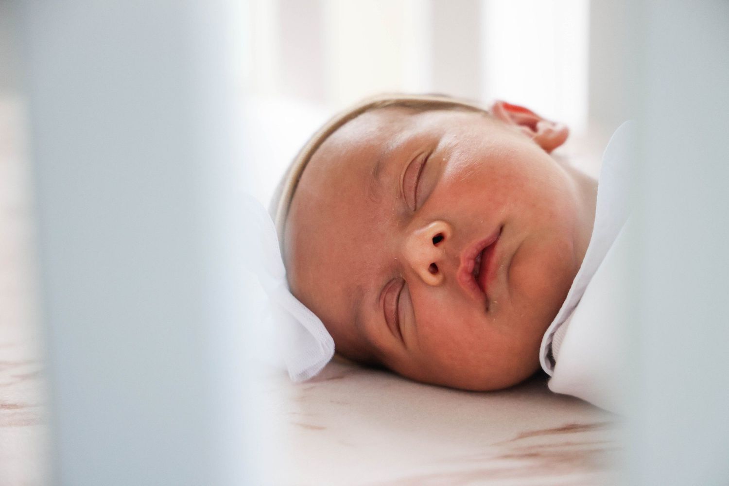 Sleeping newborn baby viewed through crib slats in soft natural light in Abilene, Texas.