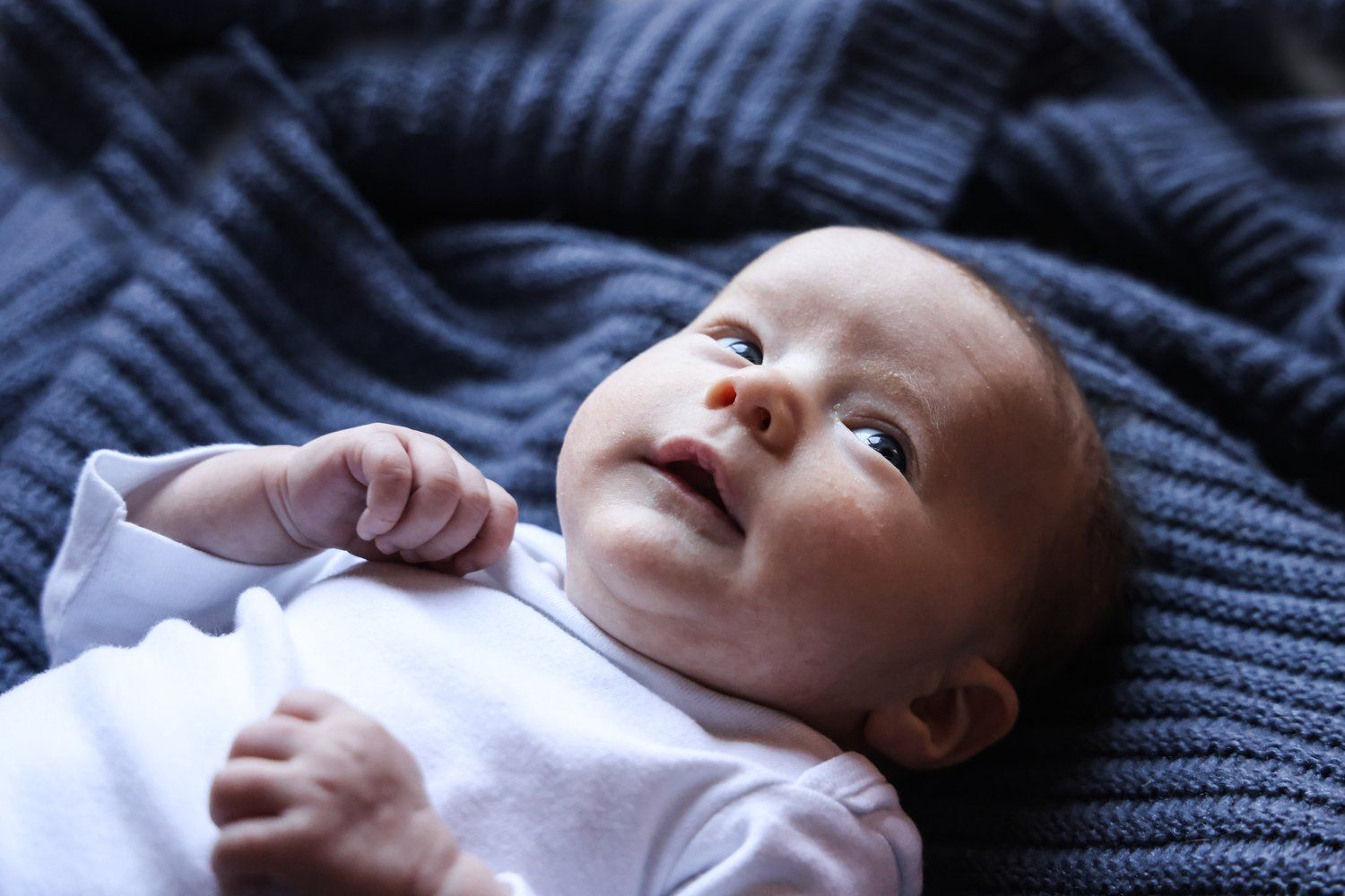 Baby in white onesie lying on blue knit blanket looking up in Abilene, Texas.