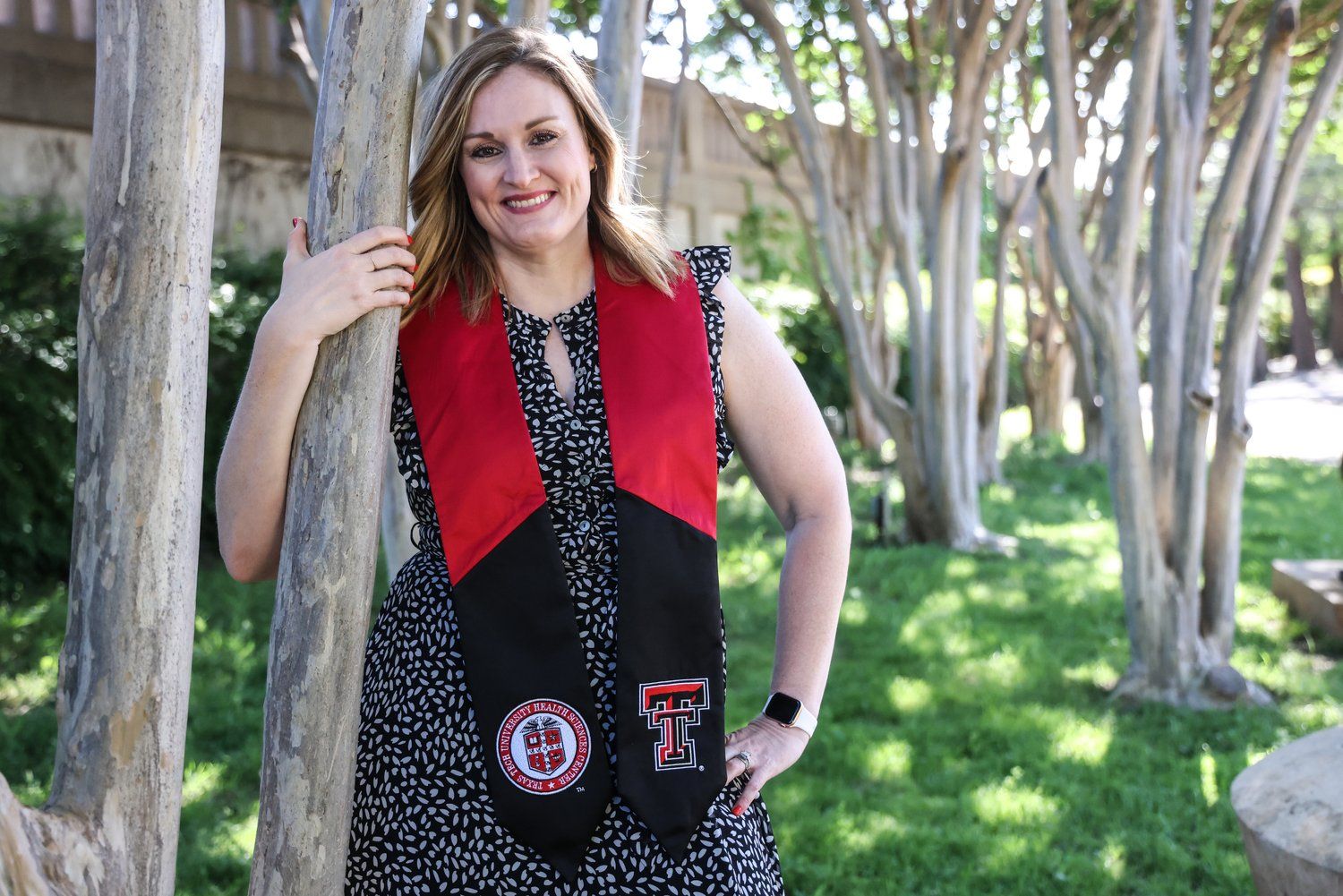 Graduate wearing polka dot dress and red stole with university insignia outdoors in Abilene, Texas.