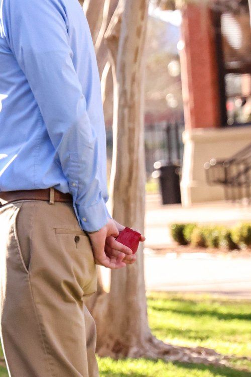 Person in blue shirt holding small red box behind their back outdoors in Abilene, Texas.