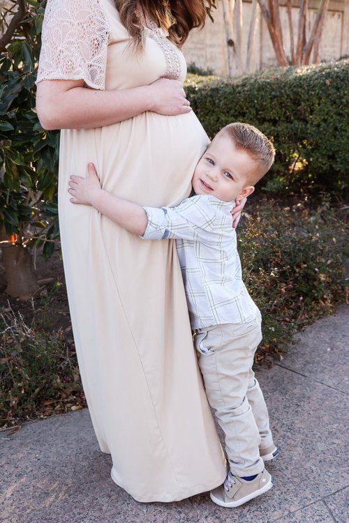 Young child hugging pregnant woman in lace dress outdoors in Abilene, Texas.