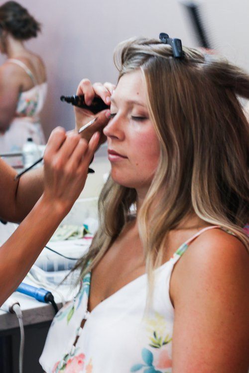 A makeup artist applies cosmetics to a bride during wedding preparations.