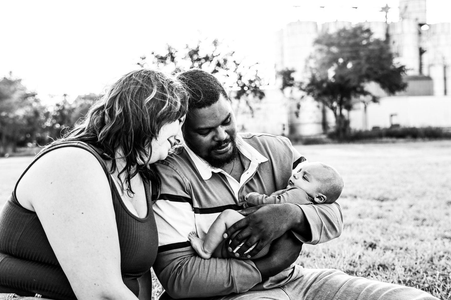 A black and white photo of parents lovingly interacting with their infant on grass outdoors in Abilene, Texas.