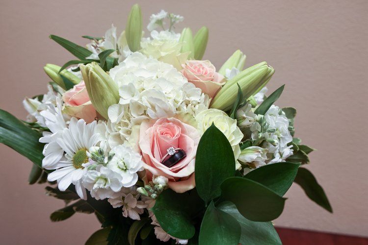 An elegant bridal bouquet with pink roses, white hydrangeas, and lilies against a neutral background.