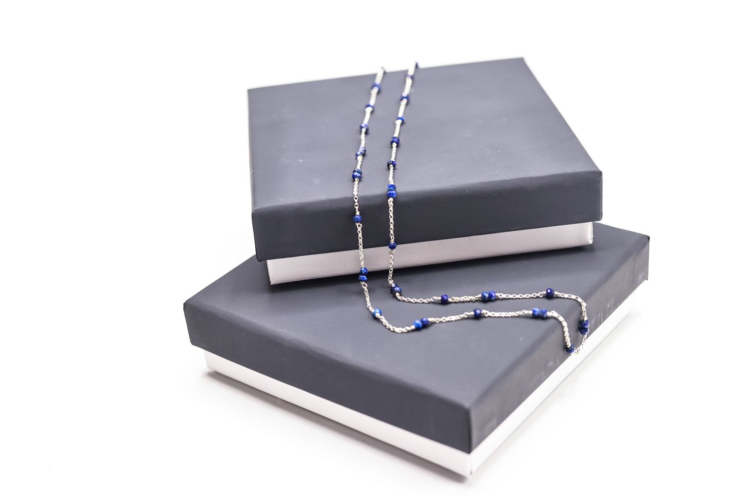 Two gray jewelry boxes stacked with delicate blue beaded necklace draped across them.