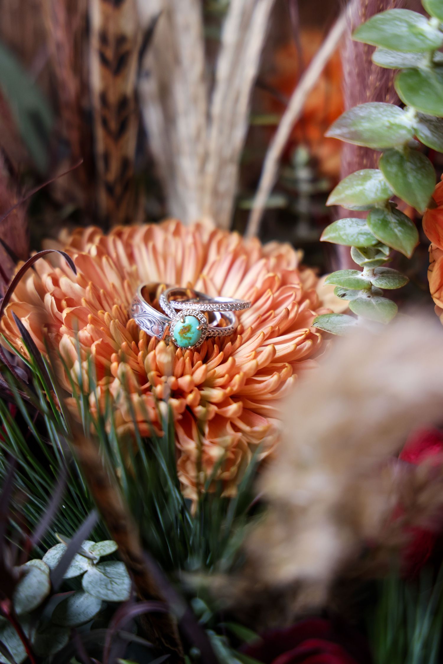Engagement ring with emerald stone displayed on an orange chrysanthemum flower.