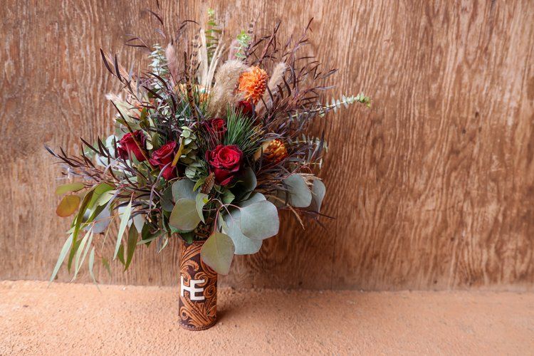 Rustic wedding bouquet with red roses, wildflowers, and eucalyptus leaves against wooden background in Abilene, Texas.