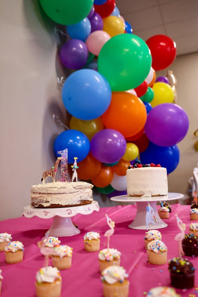 Colorful balloon arch display with birthday cakes and cupcakes on a pink table in Abilene, Texas.