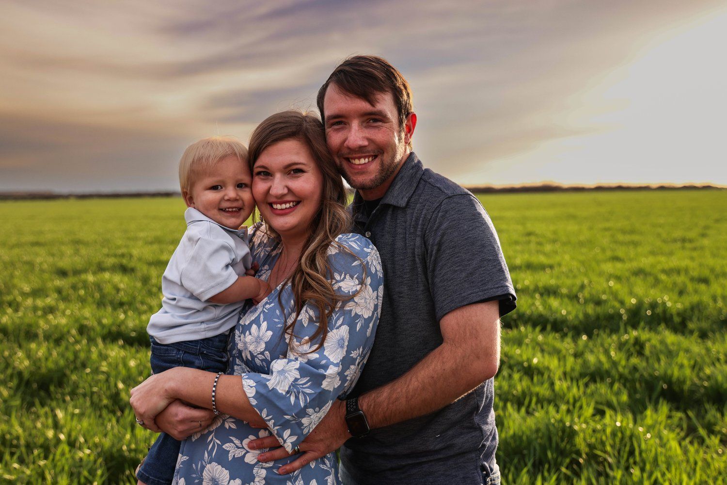 Happy family portrait in a lush green field during golden hour sunset in Abilene, Texas.