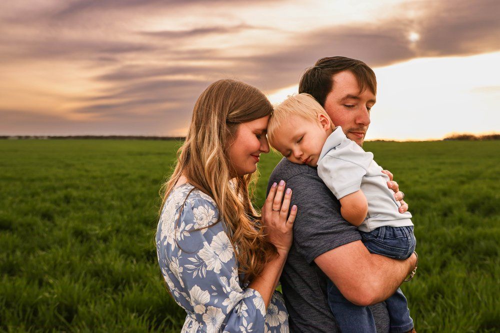 A family embraces in a green field during golden hour sunset in Abilene, Texas.