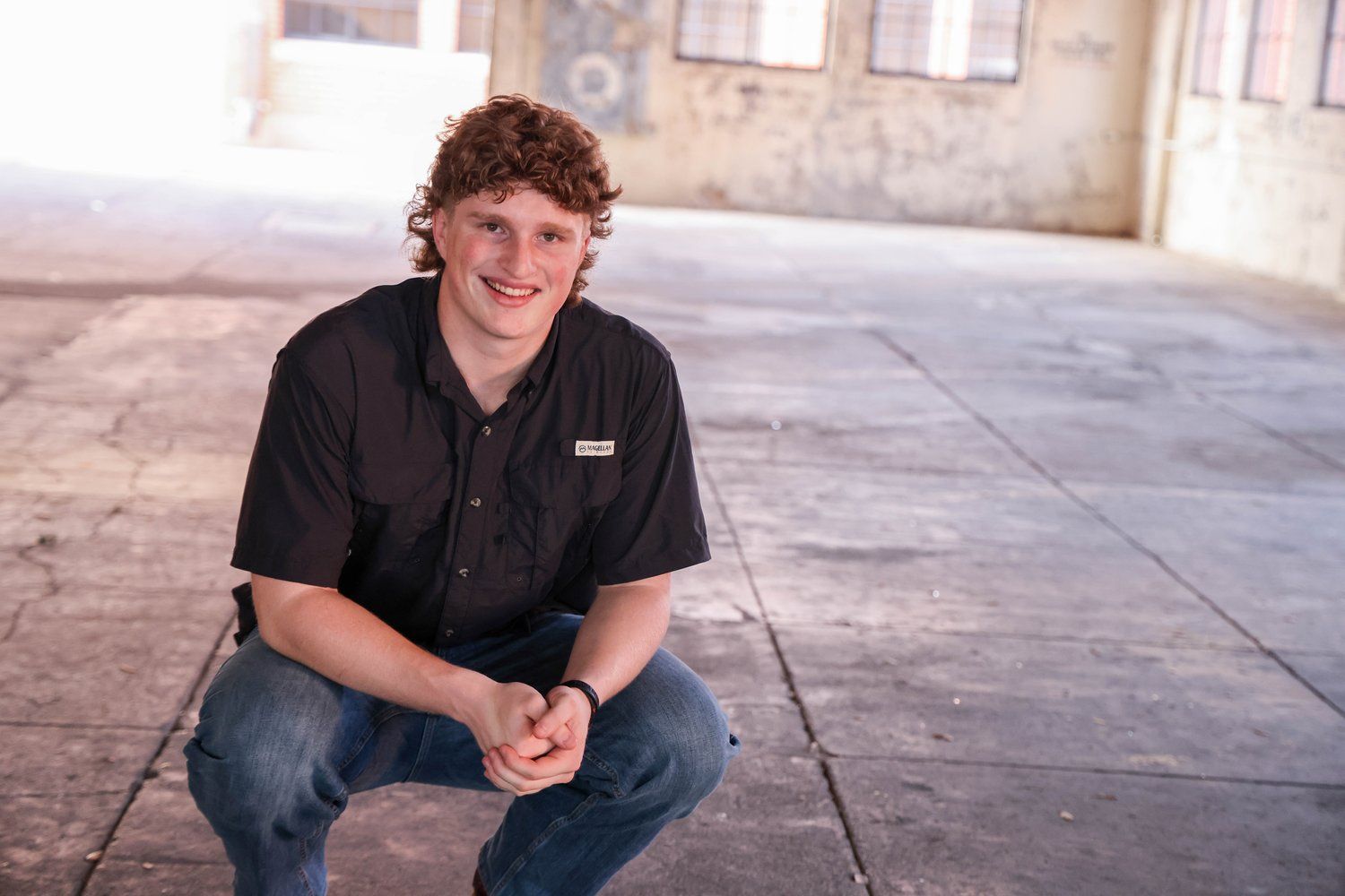 Portrait of a young person in casual attire sitting against an industrial concrete wall in Abilene, Texas.