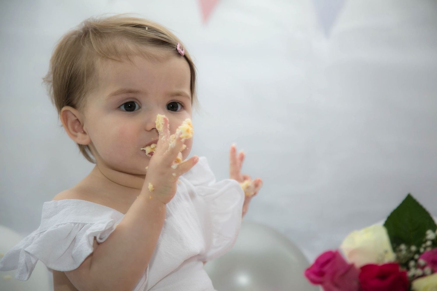 baby licking frosting from her fingers from an indoor cake smash photo session