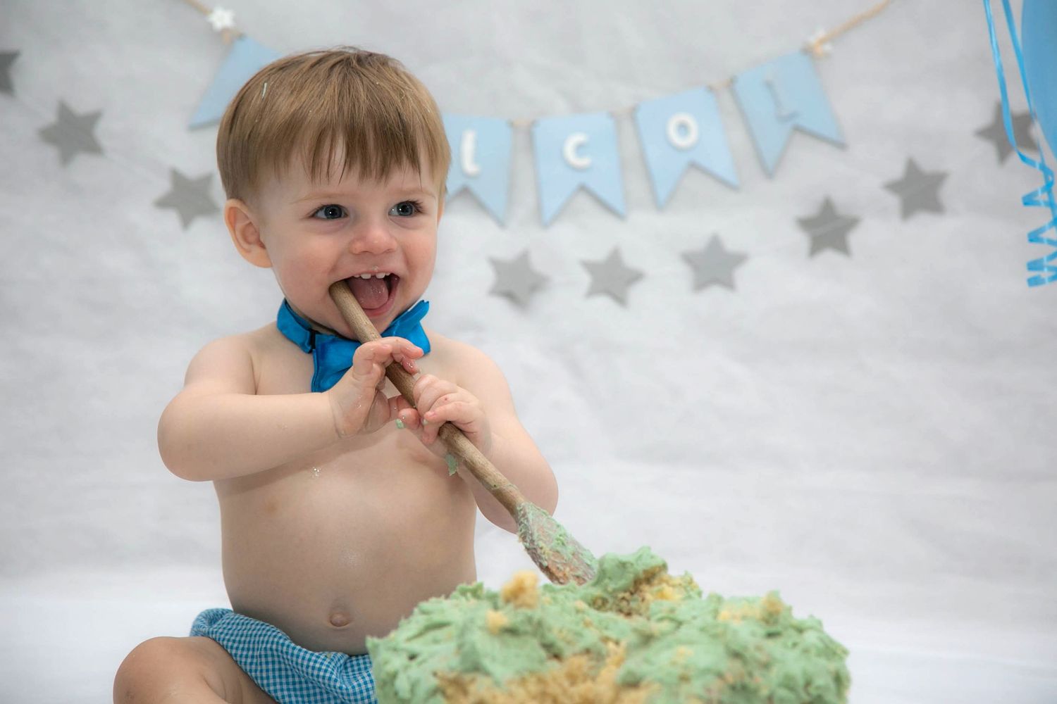 baby boy with end of wooden spoon in mouth during his indoor studio cake smash photo shoot