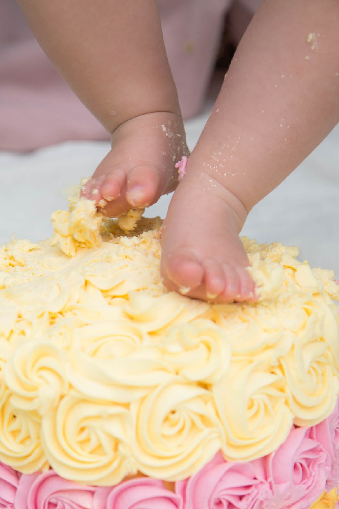 Little girl dipping her feet into her cake smash cake. Close up of baby feet exploring sensory in icing sugar