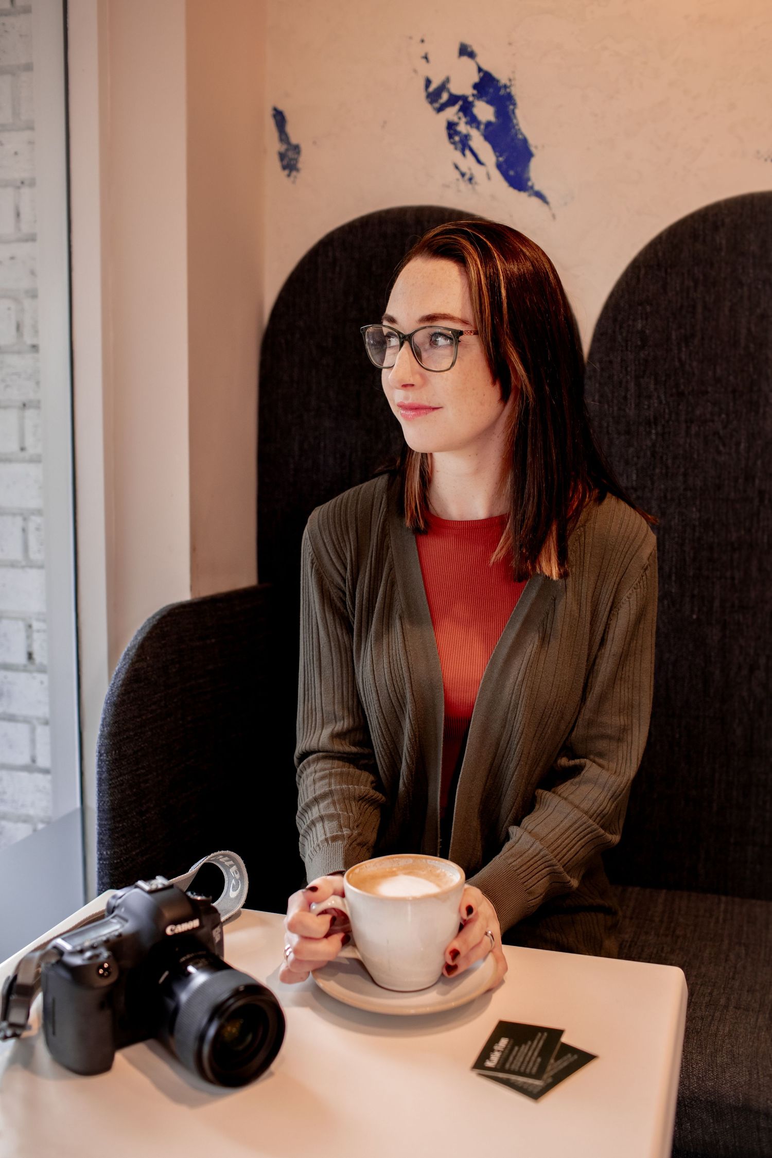 Self portrait of katie finn photography holding a coffee in hand, looking out of window. camera resting on table