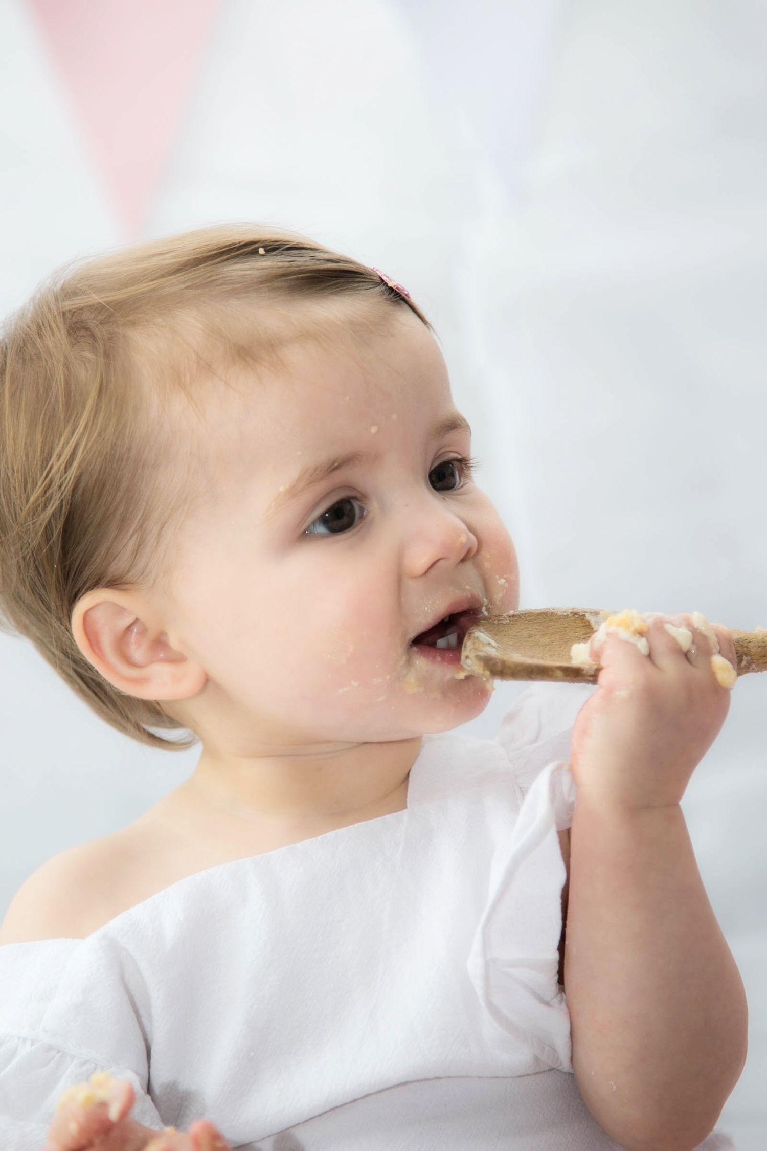 studio cake smash photo shoot. close up photo of baby licking frosting from a wooden spoon