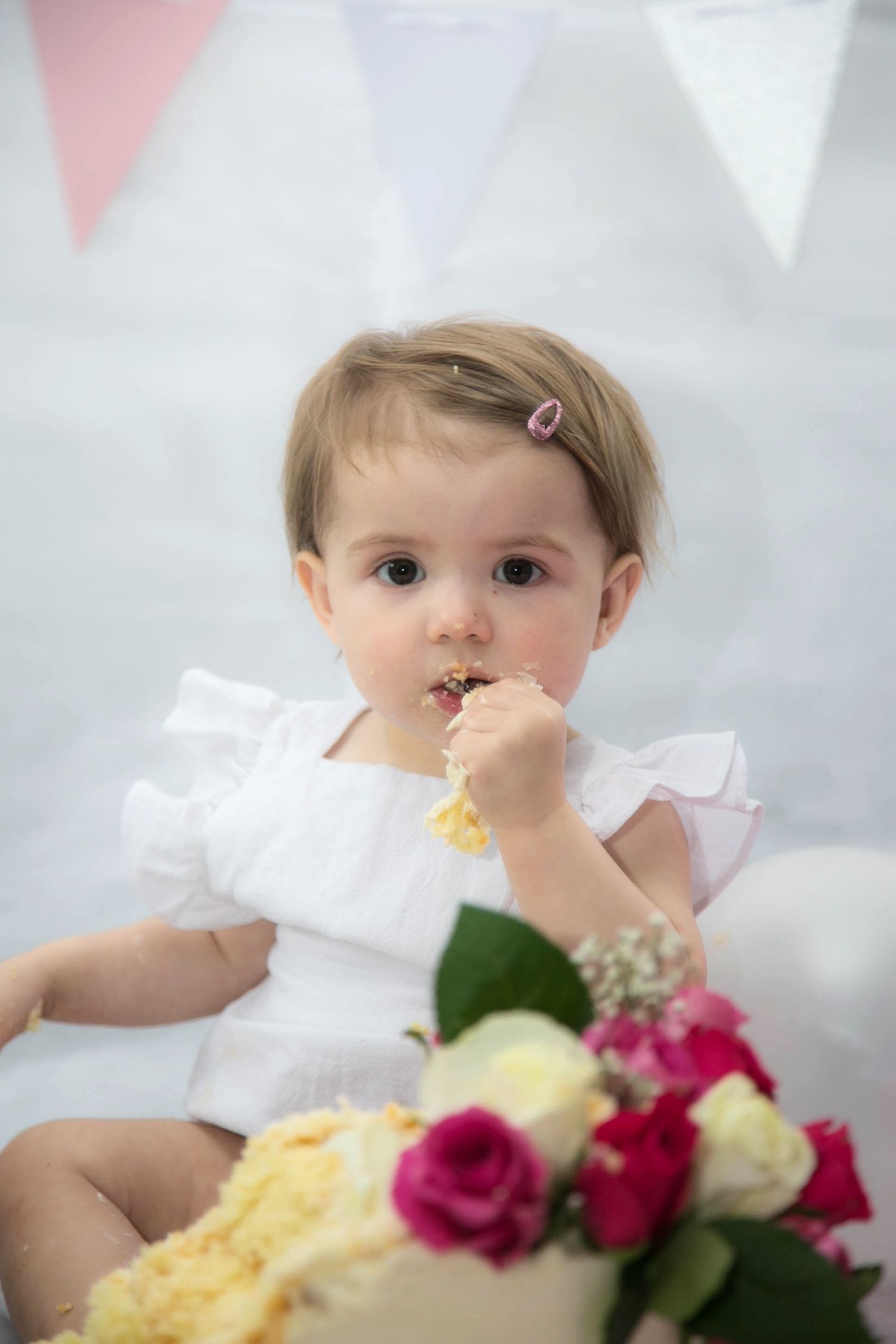 baby cake smash indoor photo shoot of baby looking into camera eating cake