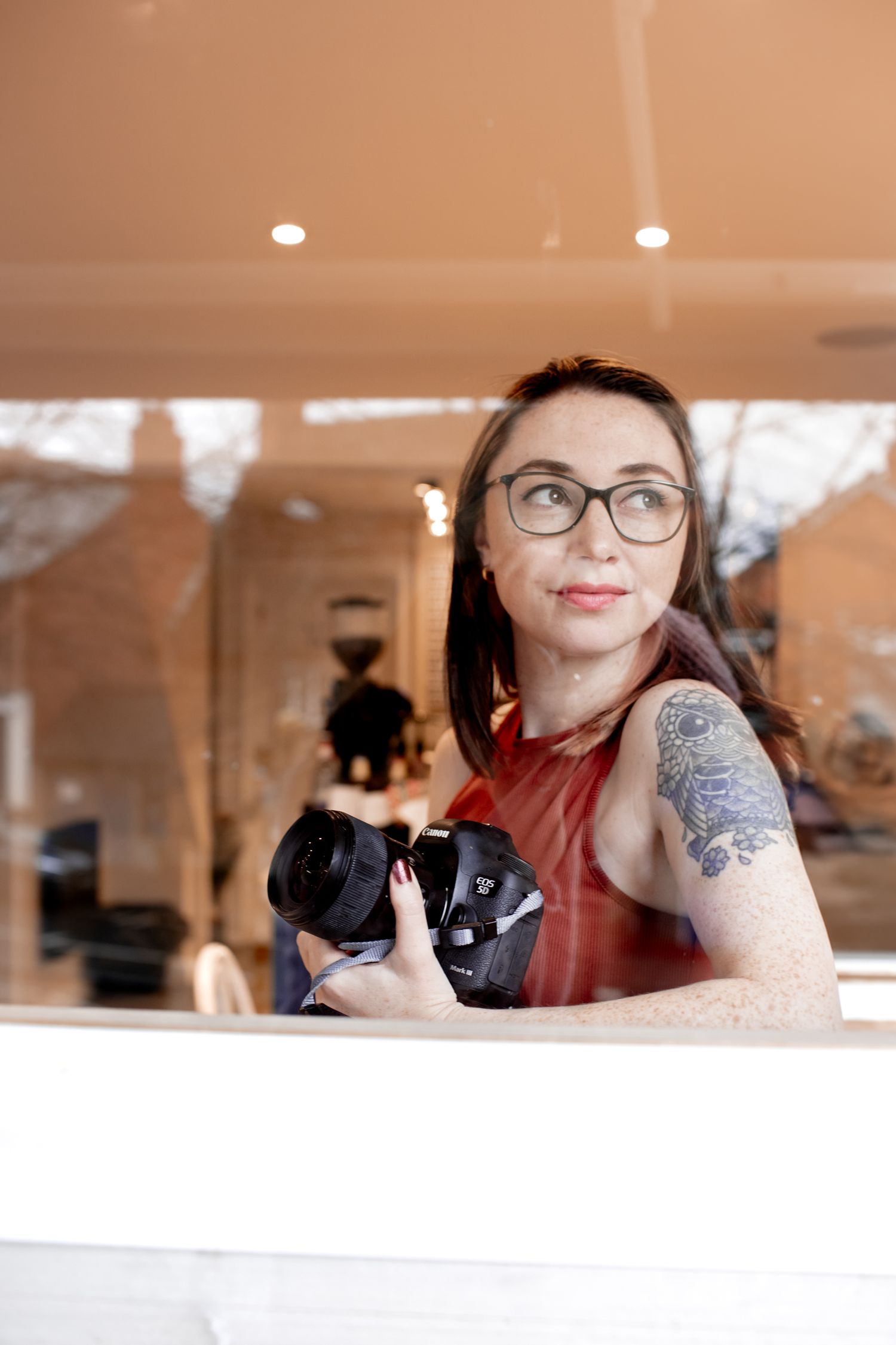 Katie Finn Photography looking out of window with reflection on her face, holding her camera