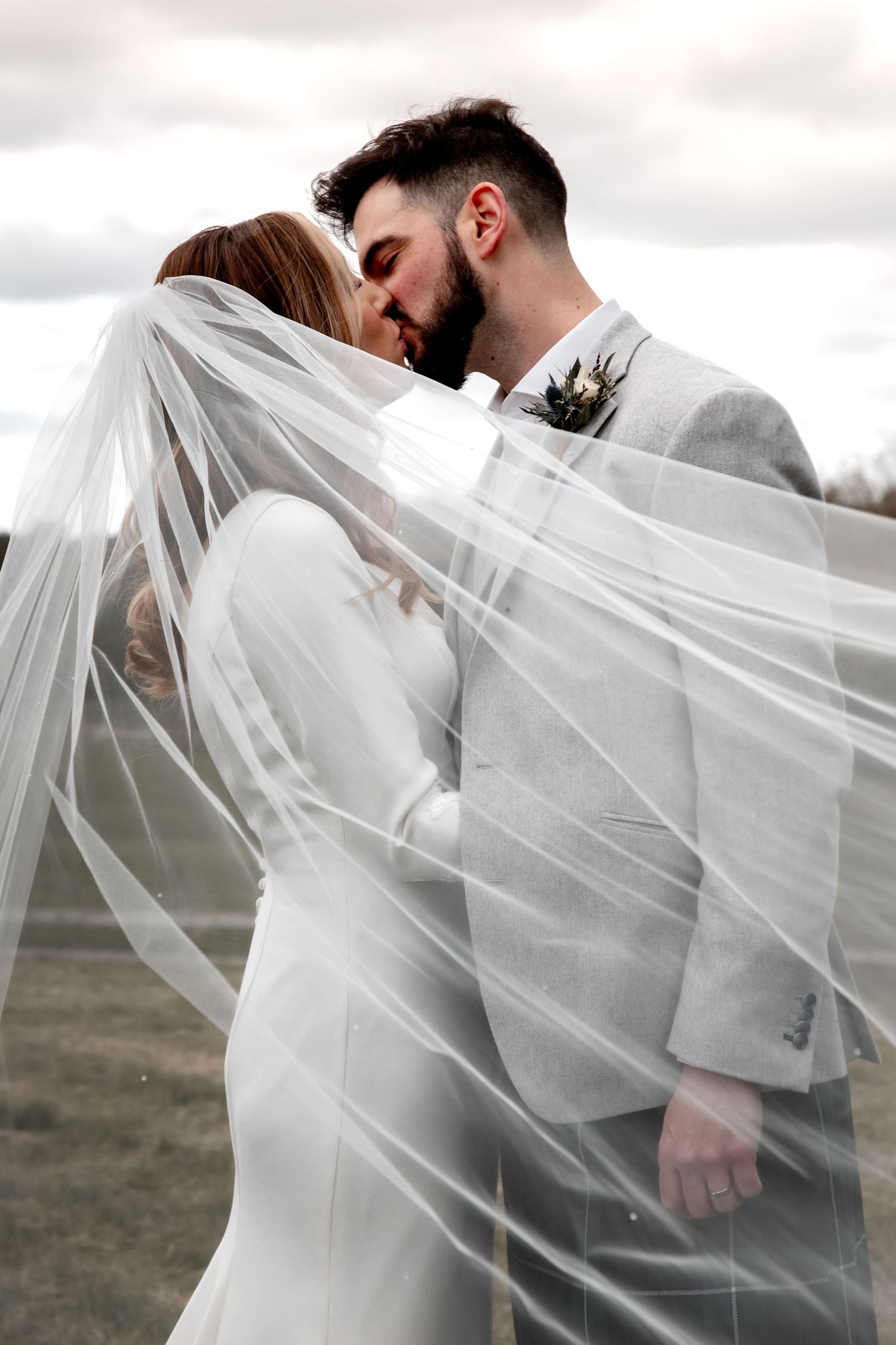 bride and groom at dodford manor kissing, with the wind blowing brides veil