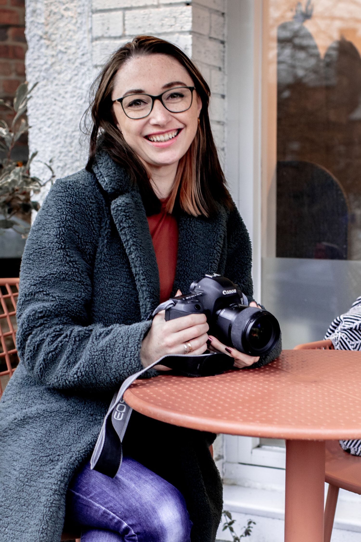 Katie Finn Photography smiling into camera, sitting outside a coffee shop holding her camera