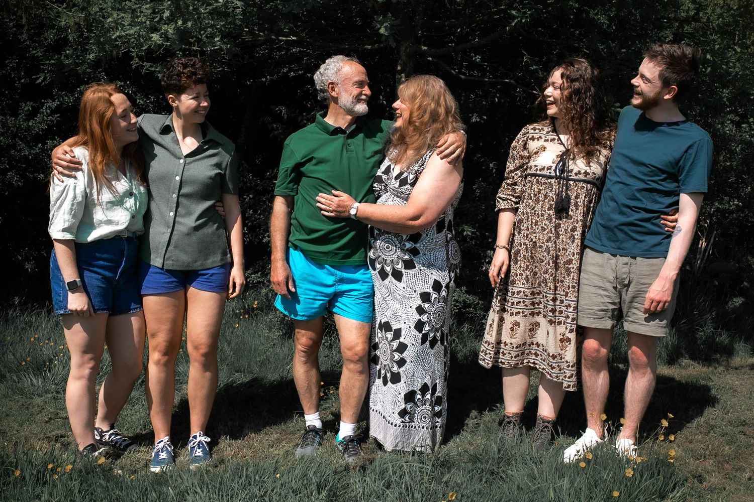 Family of six, each with their arms around their partners, smiling and looking at the parents