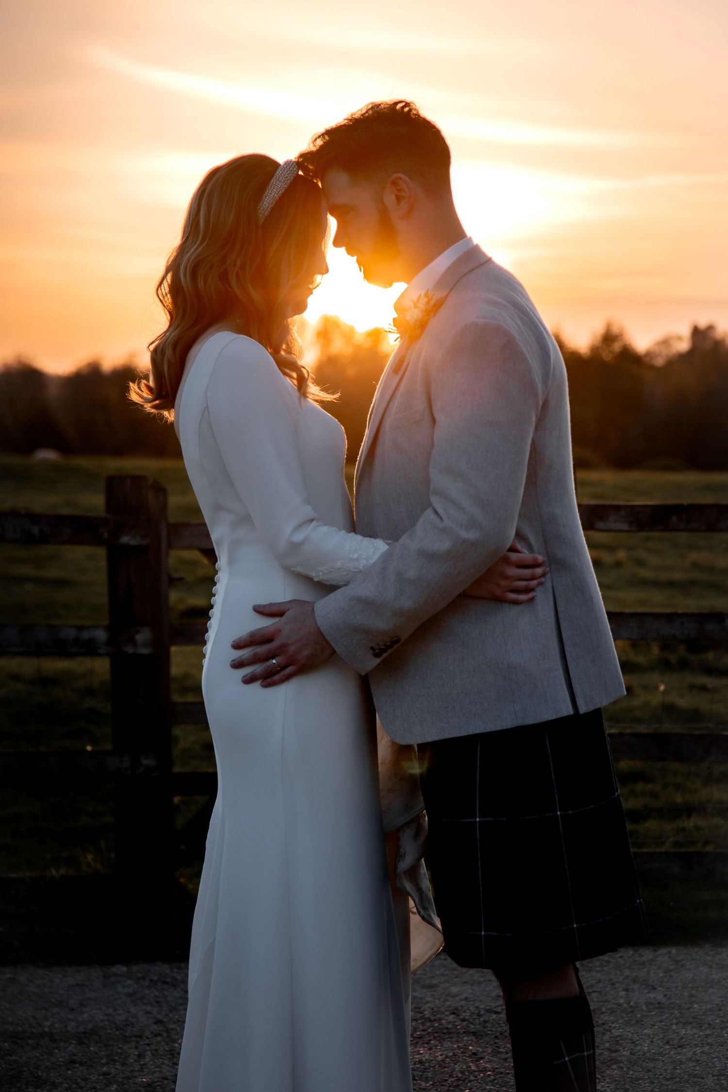 Bride and groom at Dodford Manor standing in front of sunset, touching foreheads during golden hour