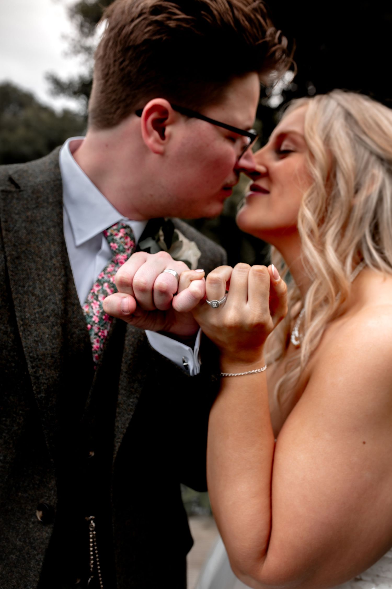 Married husband and wife share kiss, locking pinky fingers together to show off their new wedding rings