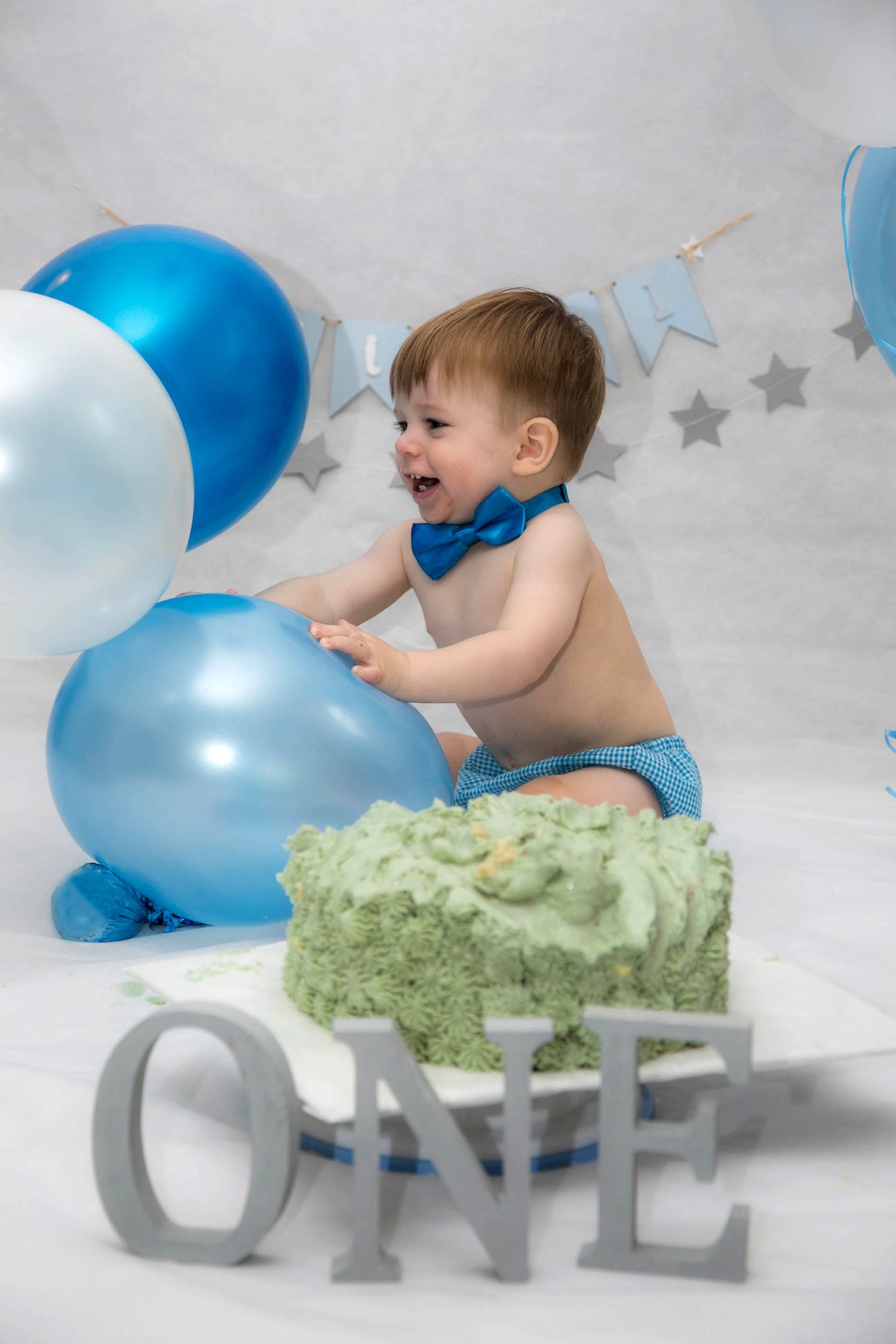 baby playing with blue balloons in his birthday cake smash photo shoot