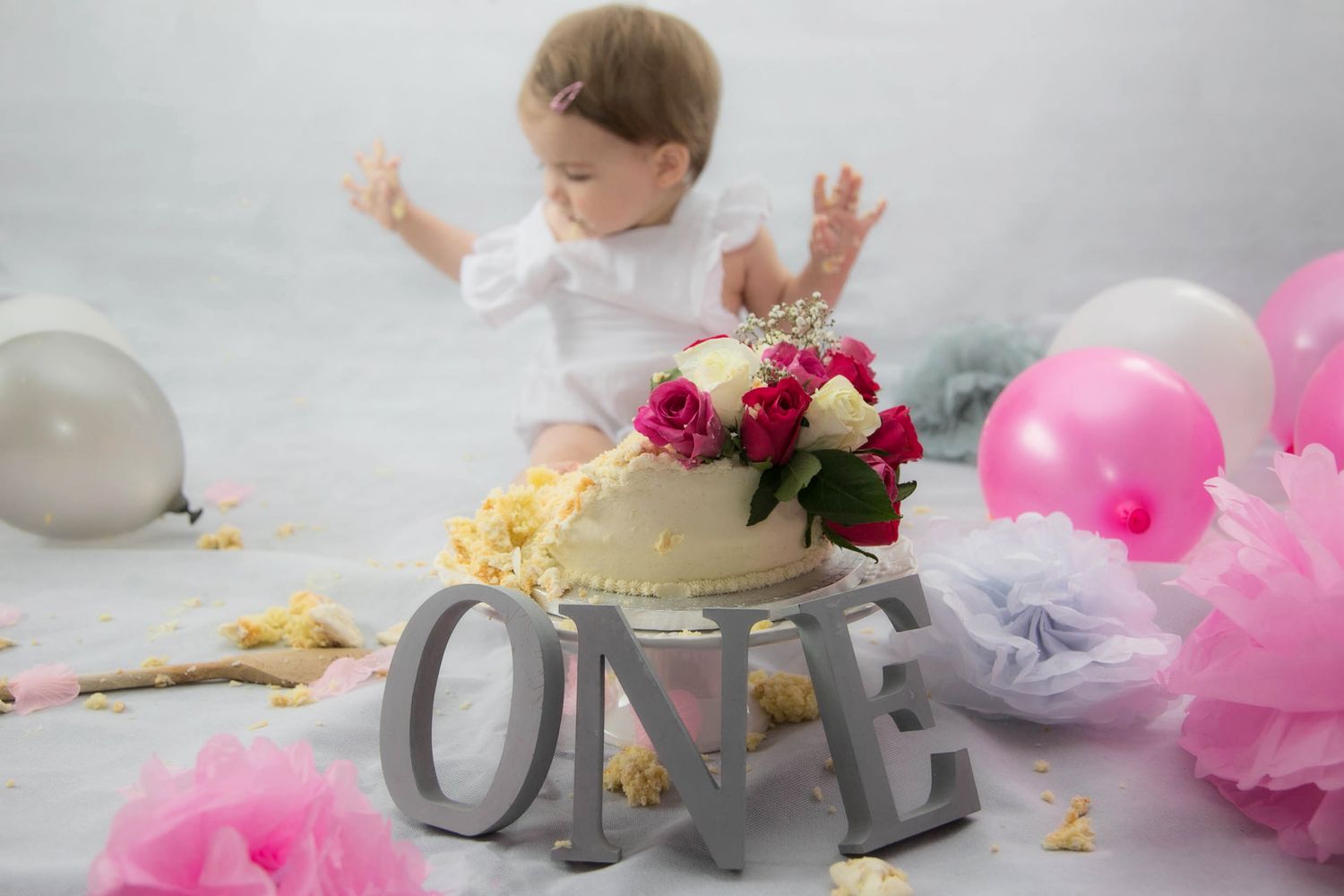 indoor studio cake smash photo shoot, baby with hands in the air, smashed cake in front of her with the letters O N E in grey